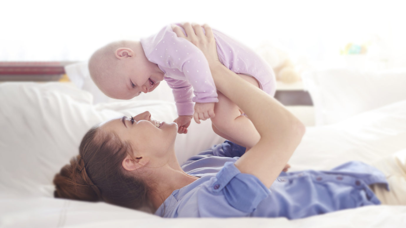 mother laying on bed while holding her baby up