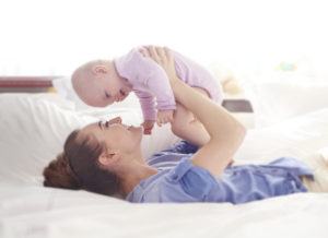 mother laying on bed while holding her baby up