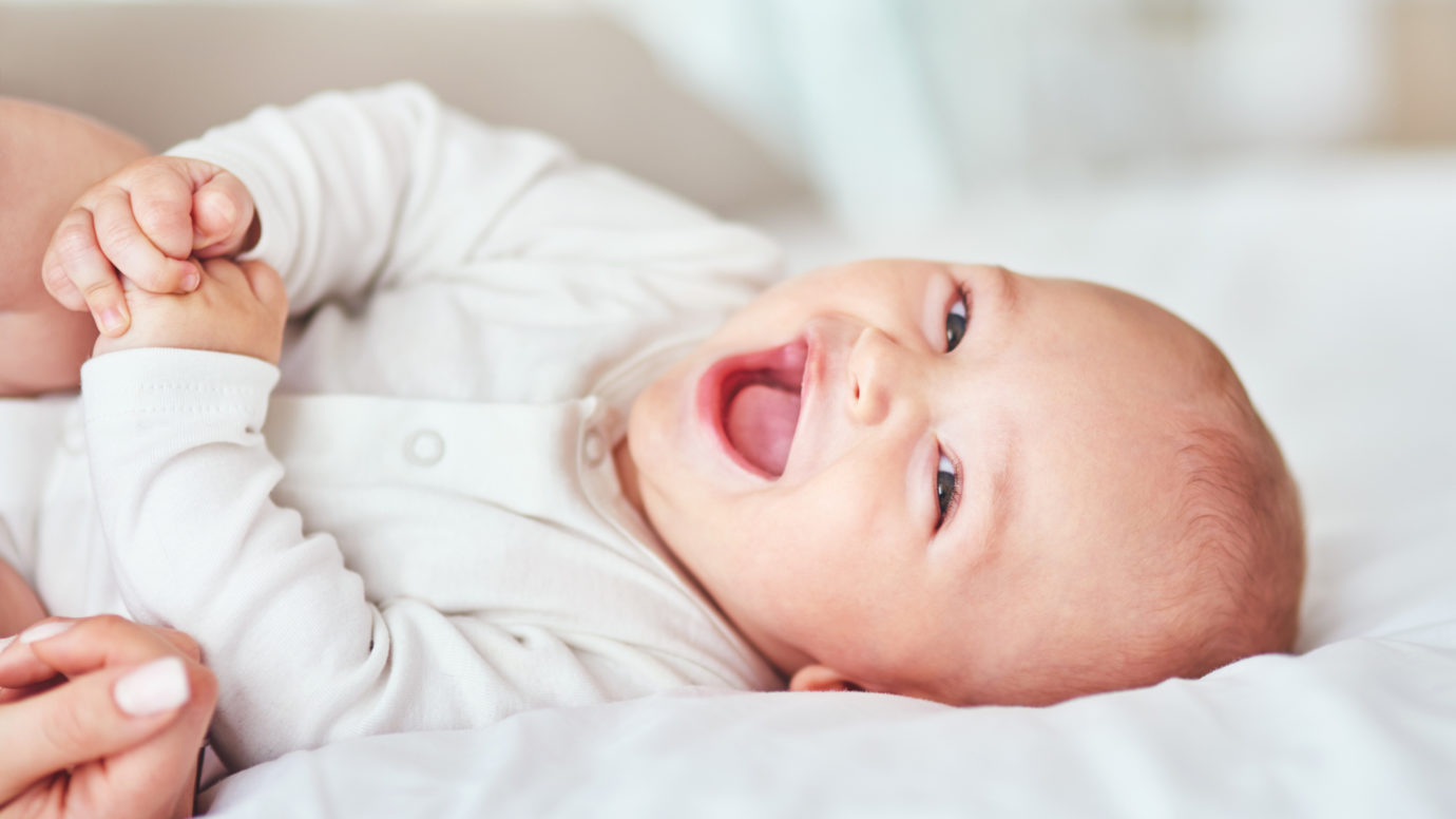 baby laughing while laying on the bed