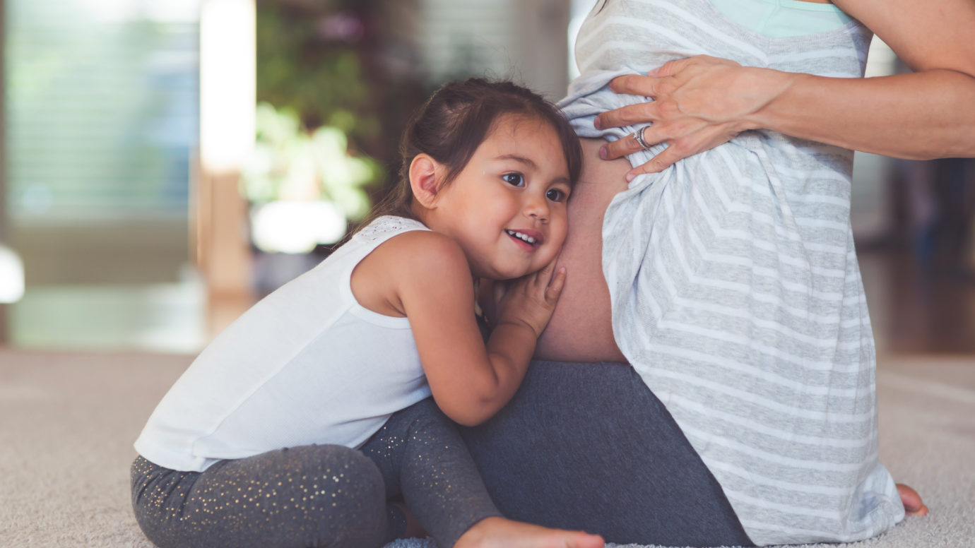 young child with her ear against pregnant mom's belly