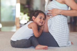 young child with her ear against pregnant mom's belly