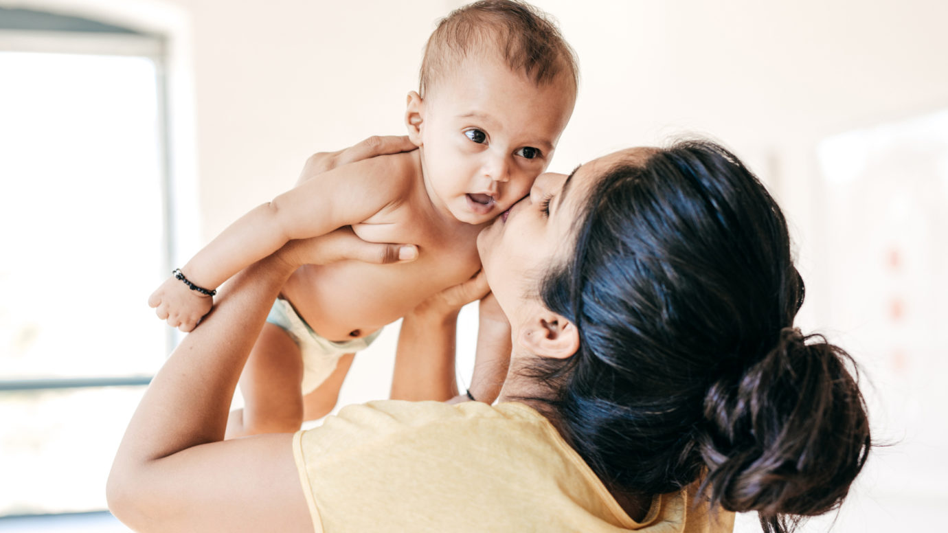 mother holding baby up and kissing his cheek