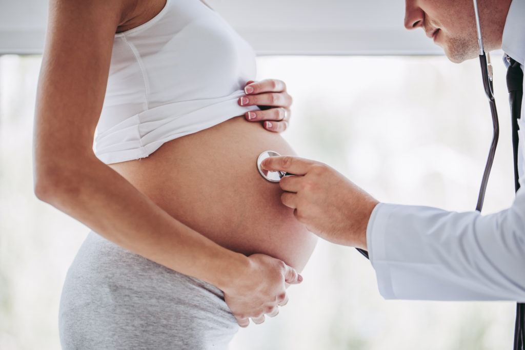 male doctor using stethoscope on pregnant women's belly