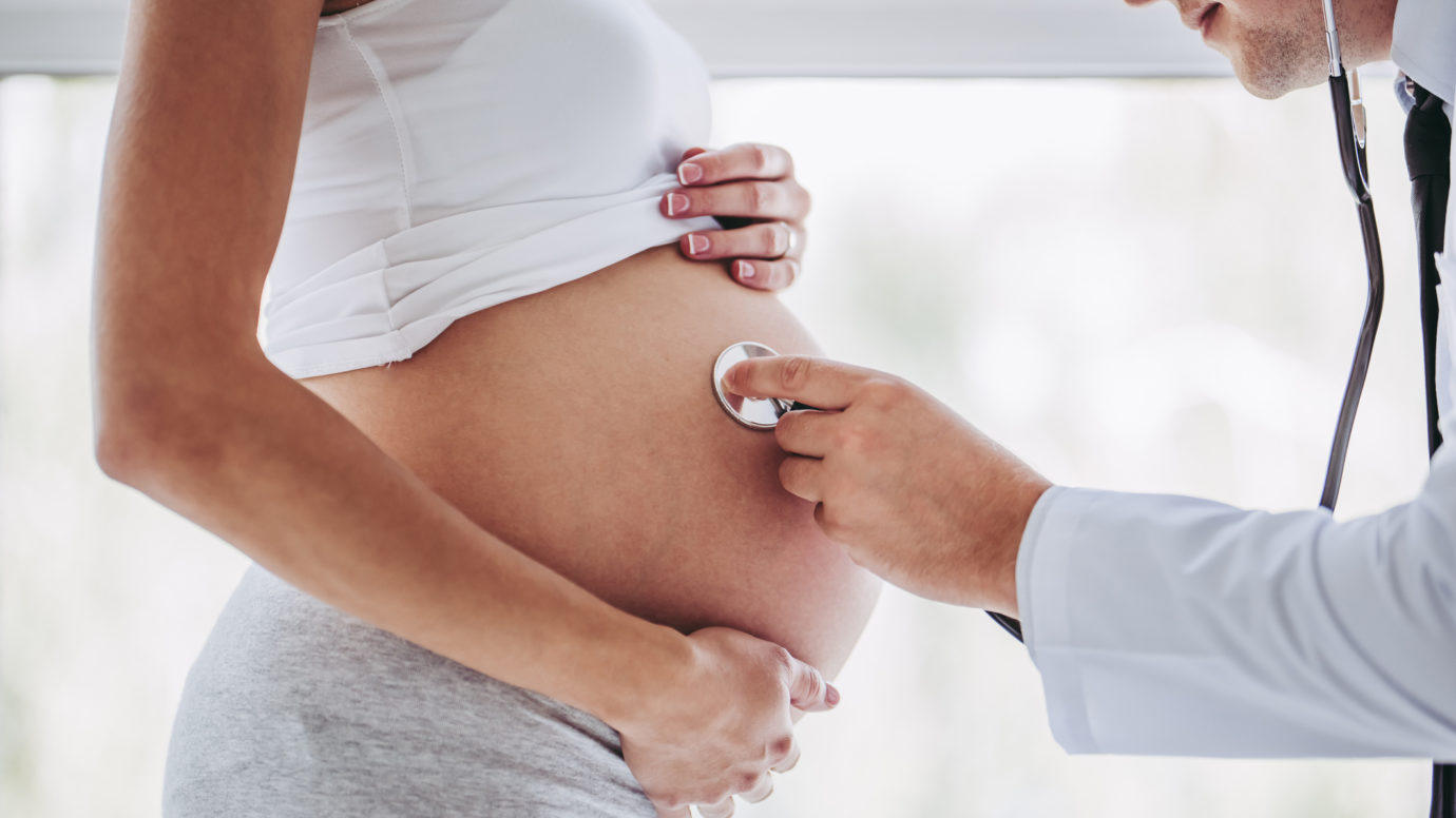 male doctor using stethoscope on pregnant women's belly